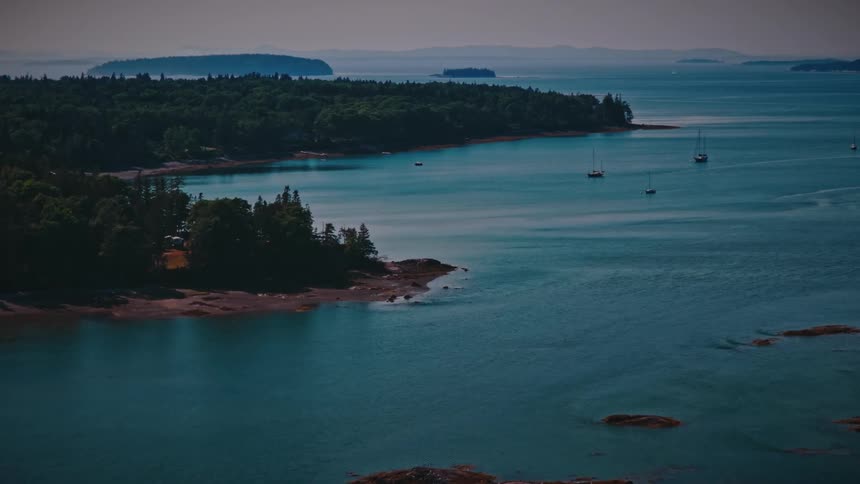 Aerial drone footage flying over a scenic bay with sailboats and forested islands on a hazy summer day