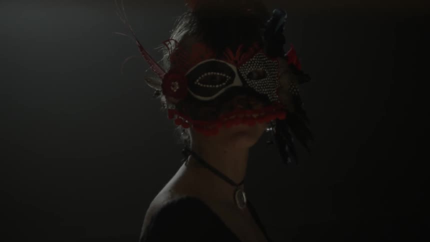 A woman wearing a mask turns in a dark room