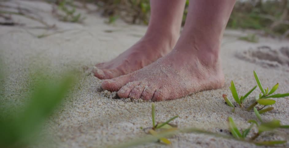 A close-up shot of a person's bare feet wiggling their toes in the soft, warm beach sand