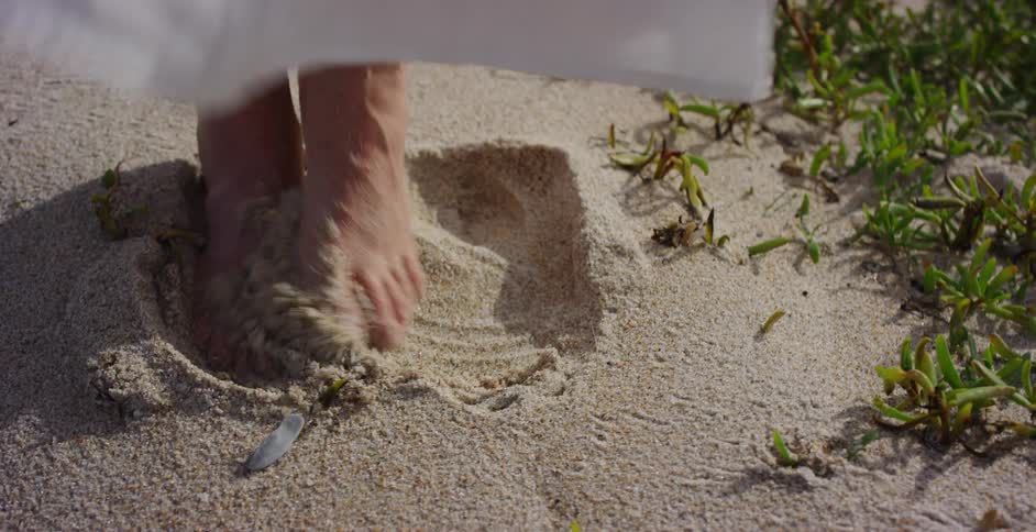 A close-up shot of bare feet wiggling and sinking into the soft, warm sand on a beach
