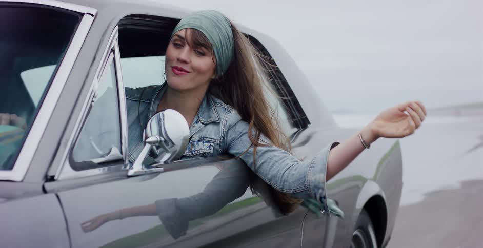 A beautiful, carefree woman leans out of her classic grey Mustang, enjoying the ocean breeze on a misty day