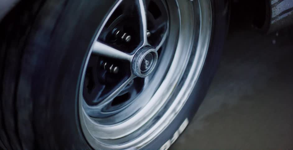 A close-up shot of a classic Ford Mustang's chrome wheel spinning as it drives down the road