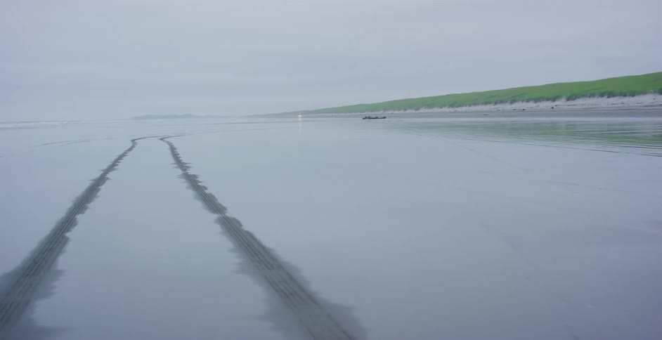 The incoming tide gently erases tire tracks left on a deserted beach on a foggy day