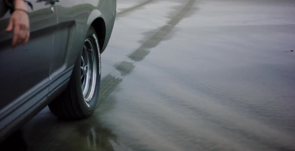 A close-up of a classic muscle car's rear wheel as the tide recedes on a wet sandy beach