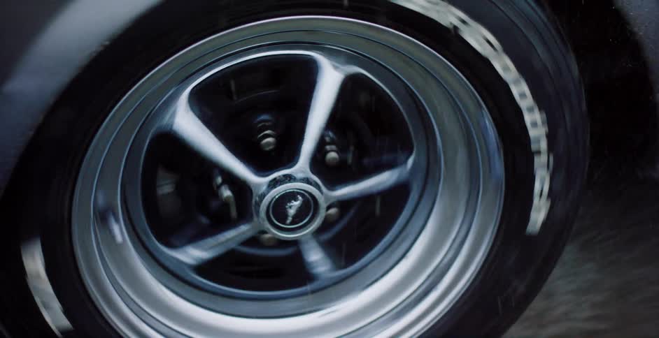 Close up slow motion shot of a classic muscle car's chrome wheel spinning on a wet road