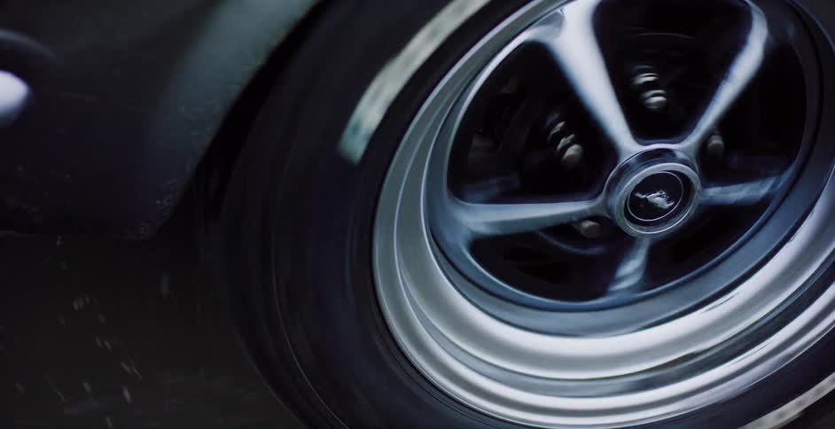 A dramatic close-up of a classic Ford Mustang's chrome wheel spinning at high speed on the road