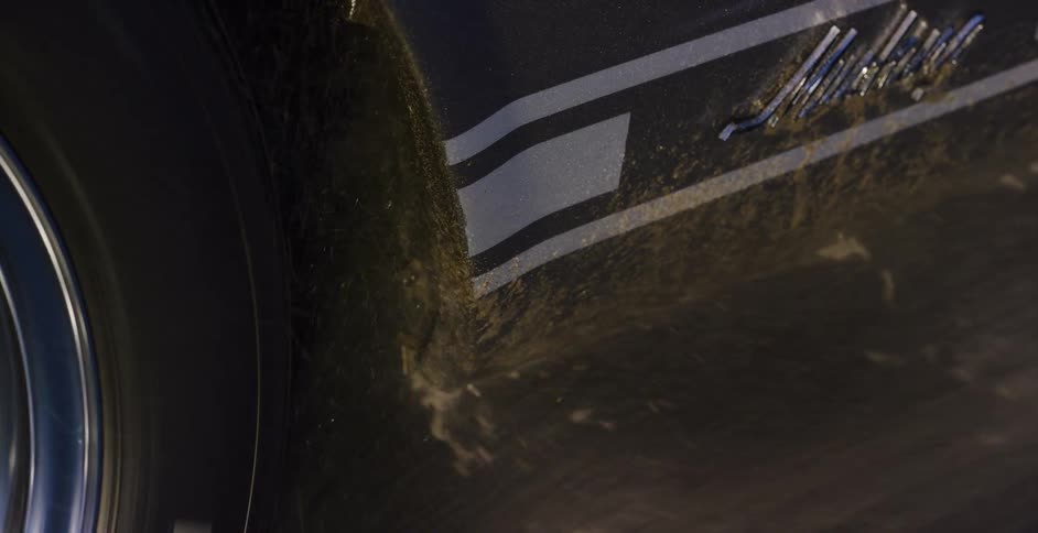 Vertical slow motion close-up of a car's spinning tire splashing mud against the side of the vehicle