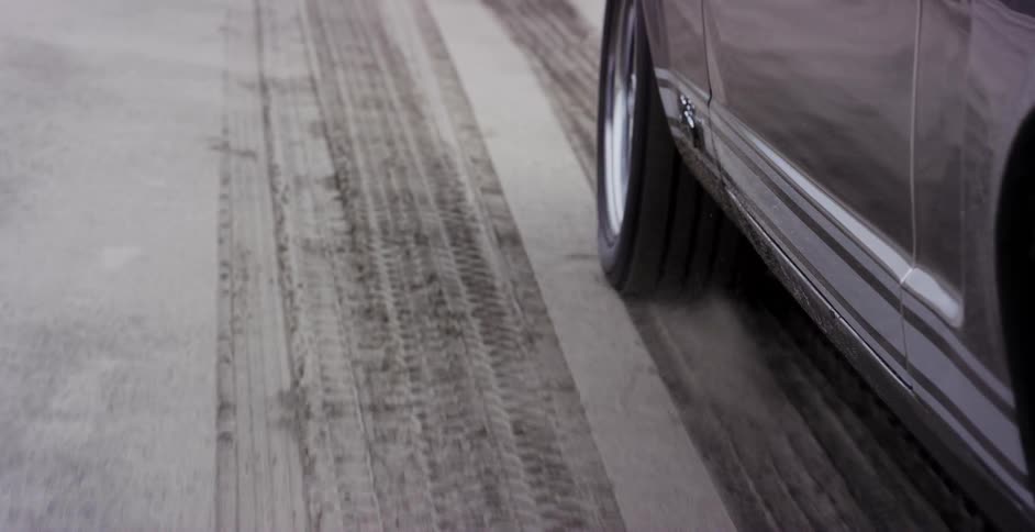 Seamless loop of a car tire spinning and kicking up sand on a dusty road
