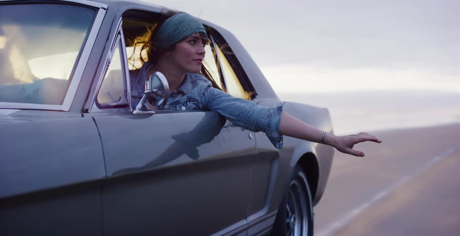 Stylish woman in a vintage car enjoys a scenic drive, feeling the breeze with her hand out the window in this cinemagraph