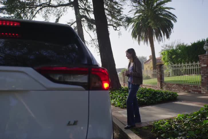 A frustrated woman waits on a suburban sidewalk for assistance after her SUV has broken down, with the hazard lights flashing