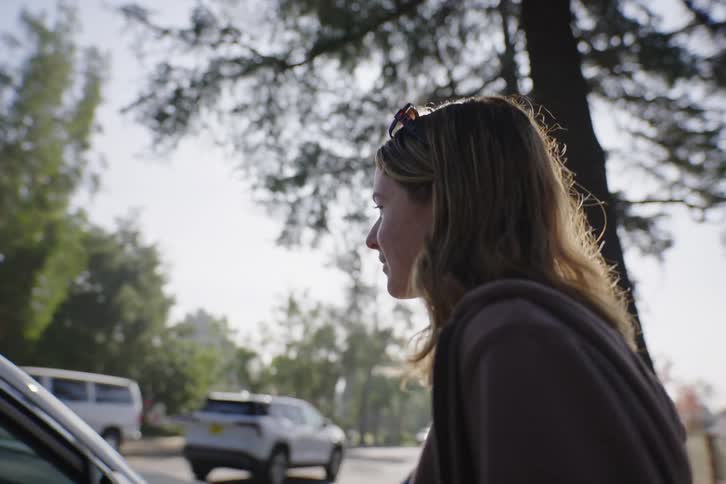 Over-the-shoulder shot of a young woman talking to her friend in a car, panning to a close-up of her smiling face on a sunny day
