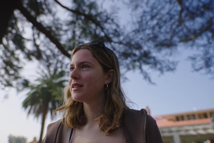 Low-angle shot of a happy young woman smiling and talking with someone off-camera in a sunny neighborhood