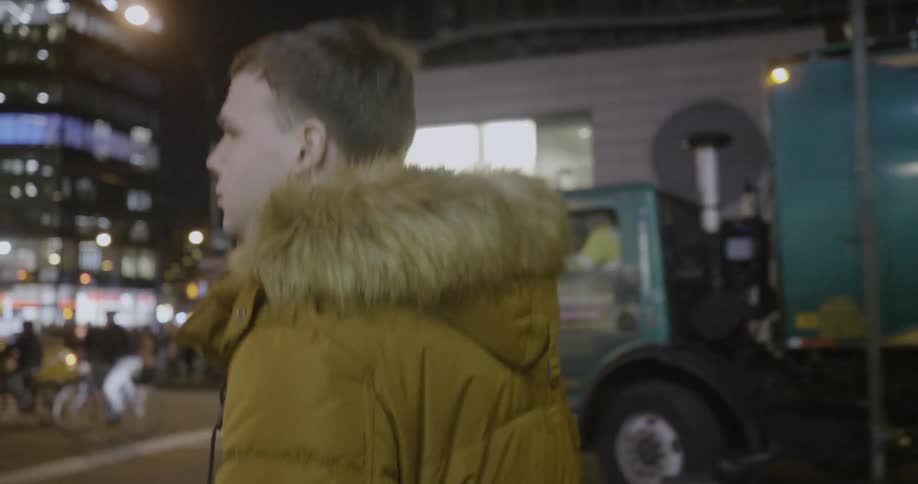 A man with a furry coat on walking through a city