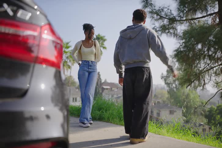A young man walks away from a young woman after a serious conversation on a sunny suburban street