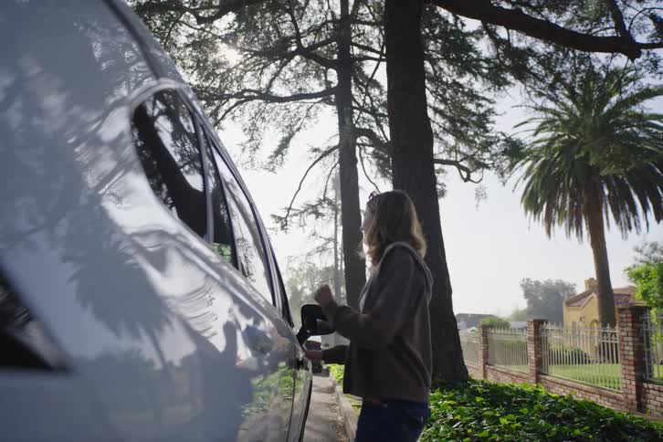 A cheerful woman happily approaches her parked car on a quiet residential street before getting inside