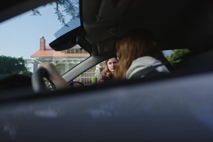 Two young women have a serious and emotional conversation through a car window in a quiet neighborhood
