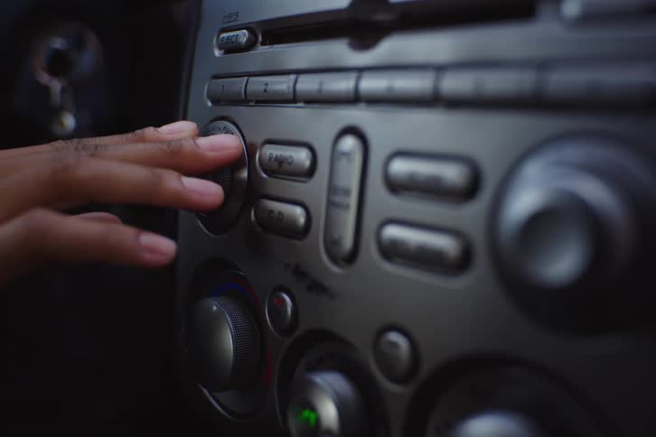 Close up of a hand turning the dials of a car stereo and climate control system
