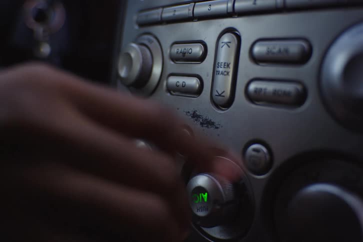 A person adjusts the radio and climate controls on the dashboard of their car