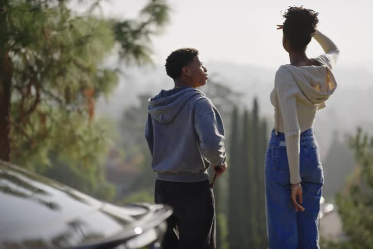 A young man gets out of his car at a scenic overlook and dances while his girlfriend records him on her phone