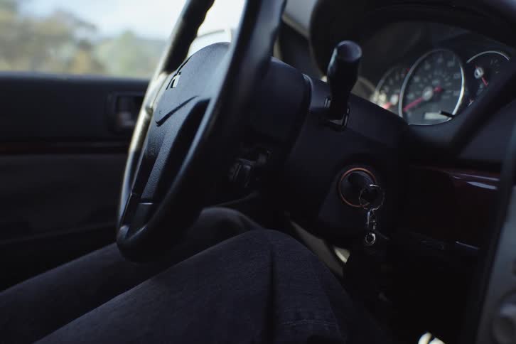 A person struggles to start their car, repeatedly turning the key in the ignition without success