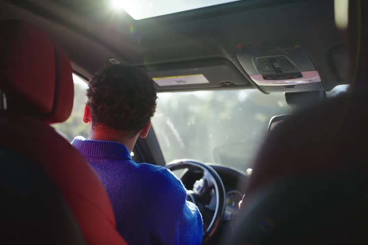 A focused young man learns how to drive from an instructor in a modern car, with sunlight streaming through the sunroof