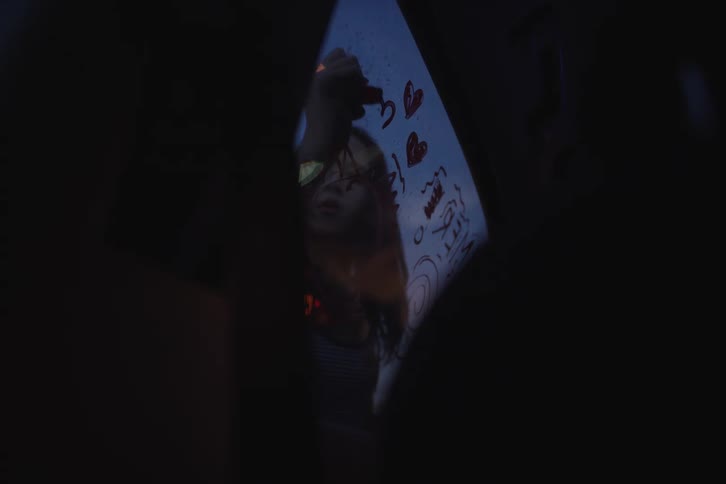 Reflection of a creative young girl drawing doodles and hearts with a red marker on a car window during a nighttime ride