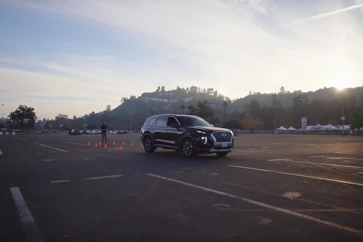 A black SUV with its hazards on is parked in a large lot at sunrise while a go-kart drives past in the background