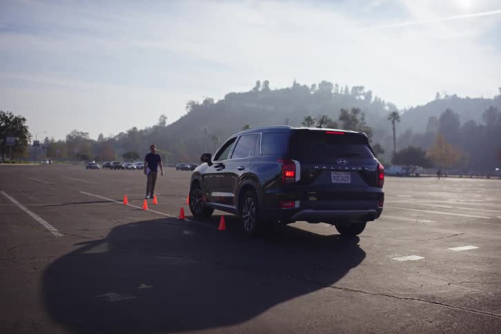 A man remotely backs a black SUV out of a parking space using the smart park assist feature on the key fob