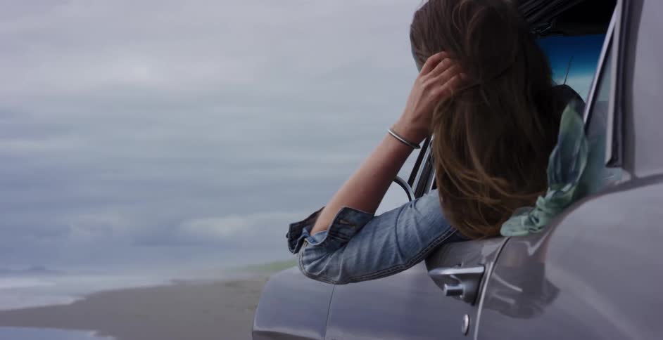 Slow motion shot of a woman's hair blowing in the wind as she leans out of her car window at the beach