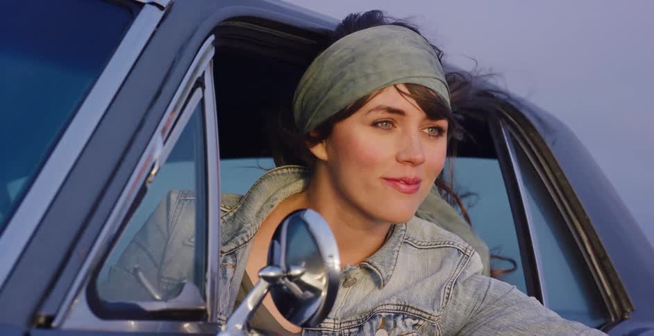 A free-spirited woman with a bandana smiles as the wind blows through her hair while she leans out of a classic car window