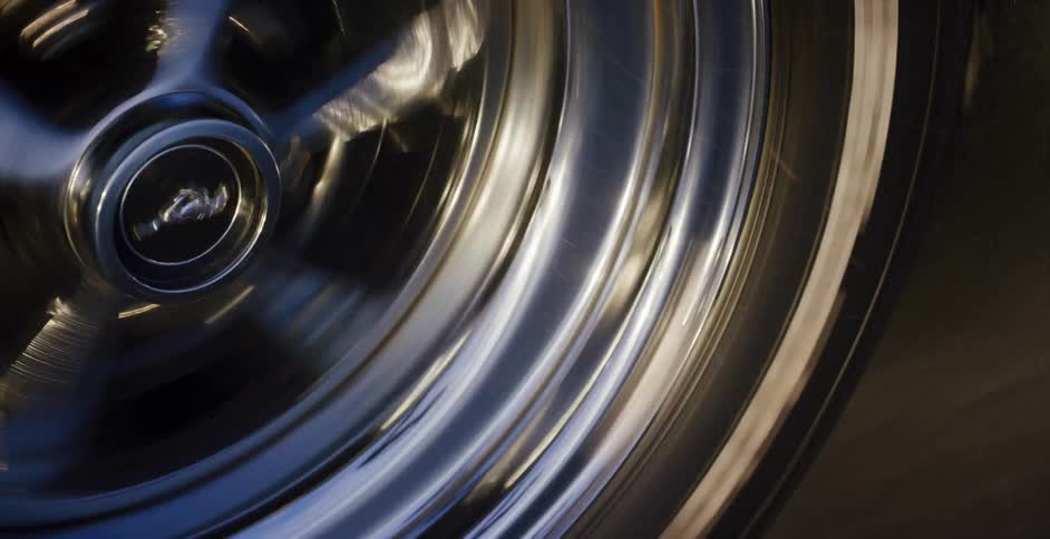 A close-up of a classic car's chrome wheel spinning rapidly, creating a dynamic motion blur as it speeds down the road
