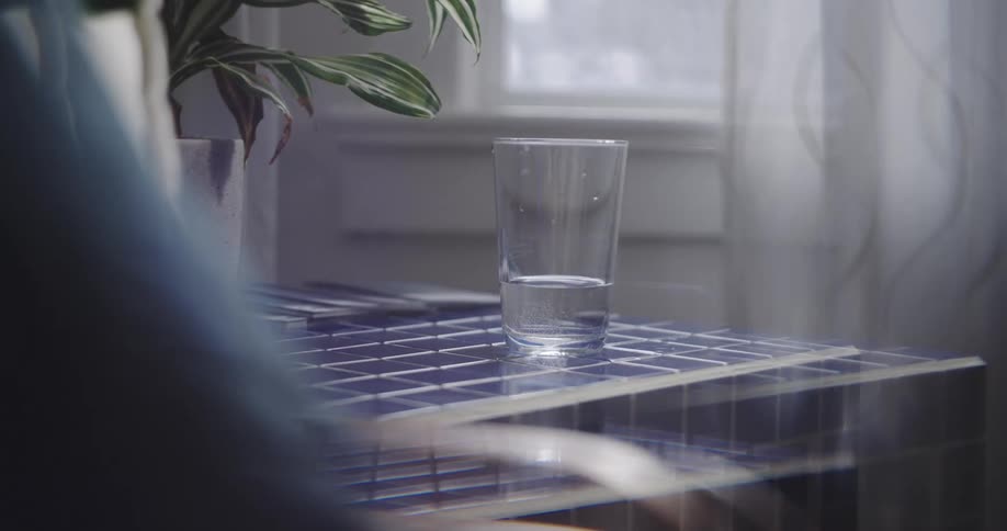 A surreal and disorienting visual effect warps the image of a glass of water on a blue tiled table