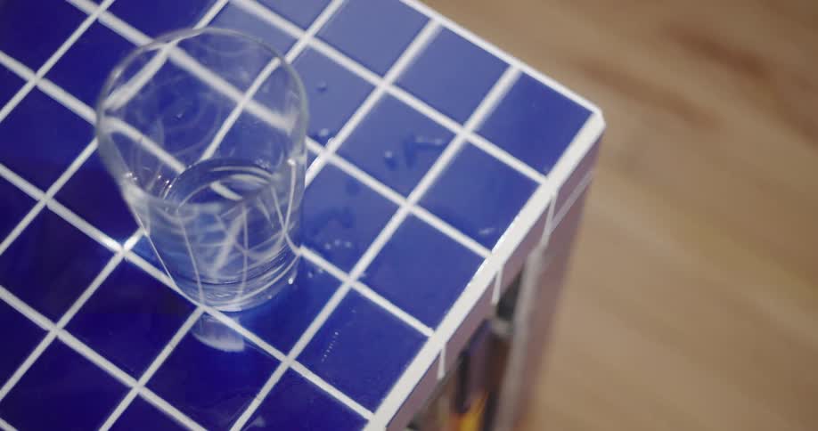 A glass of water on a blue tiled surface begins to tremble and ripple, suggesting an earthquake or tremor