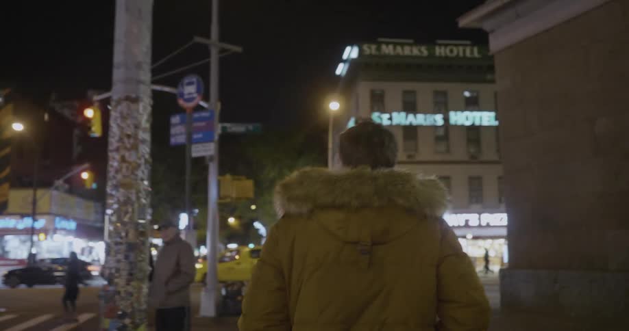 A man in a heavy coat walks on a city sidewalk at night