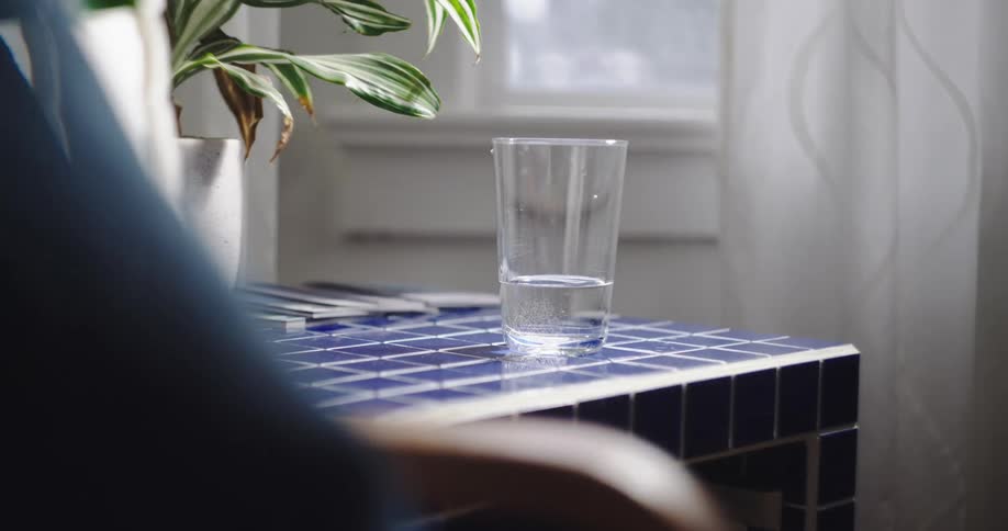 A still shot of a glass of water on a blue tiled table creates beautiful refractions of light in a sunlit room