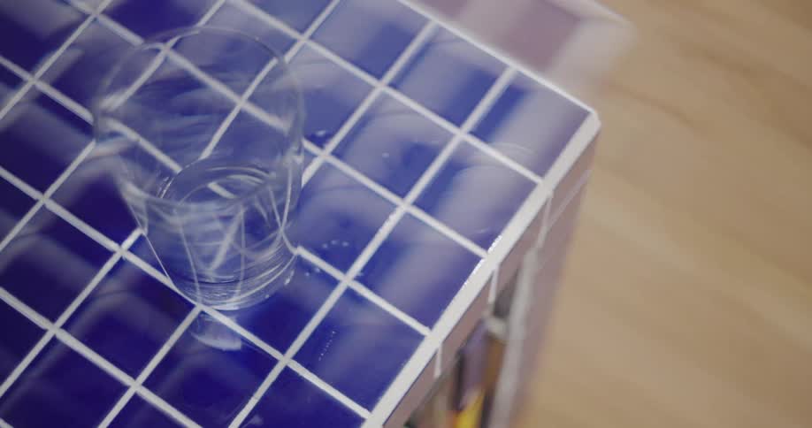 A static high-angle shot of a drinking glass with water resting on a blue tiled surface