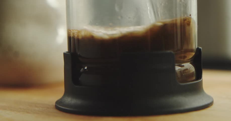A close-up slow-motion shot of hot water being poured over coffee grounds to brew coffee in a French press