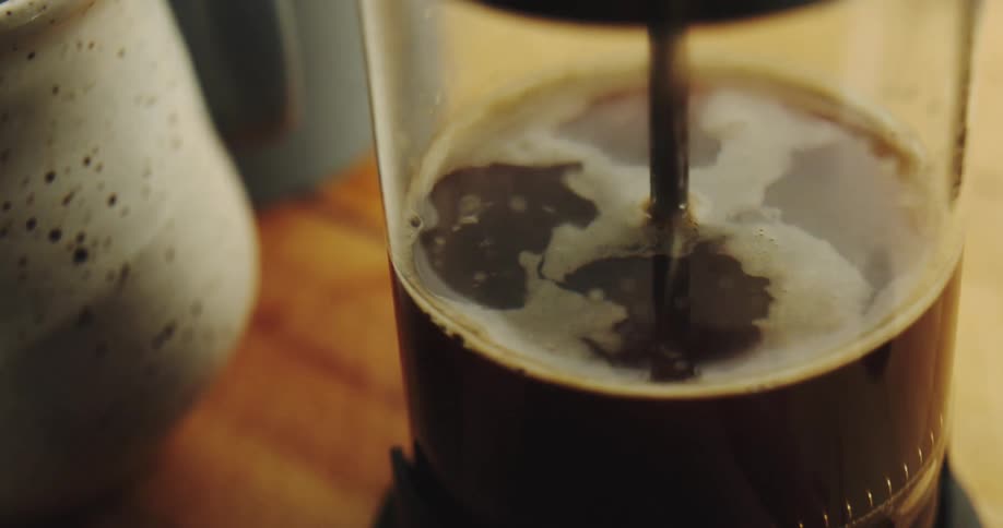 A close-up slow-motion view of a French press plunger being pushed down to brew coffee