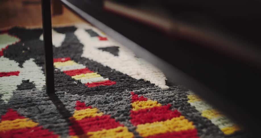A close-up of a person's sock-clad foot walking past on a colorful patterned rug in a dimly lit room
