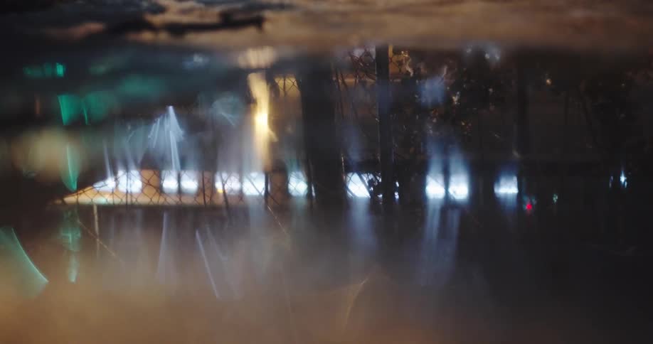 Cars and city lights create a dreamy, abstract reflection in a puddle on a snowy winter night