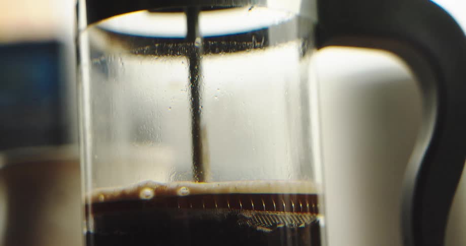 A close-up shot shows the plunger of a French press being slowly pushed down, filtering the coffee