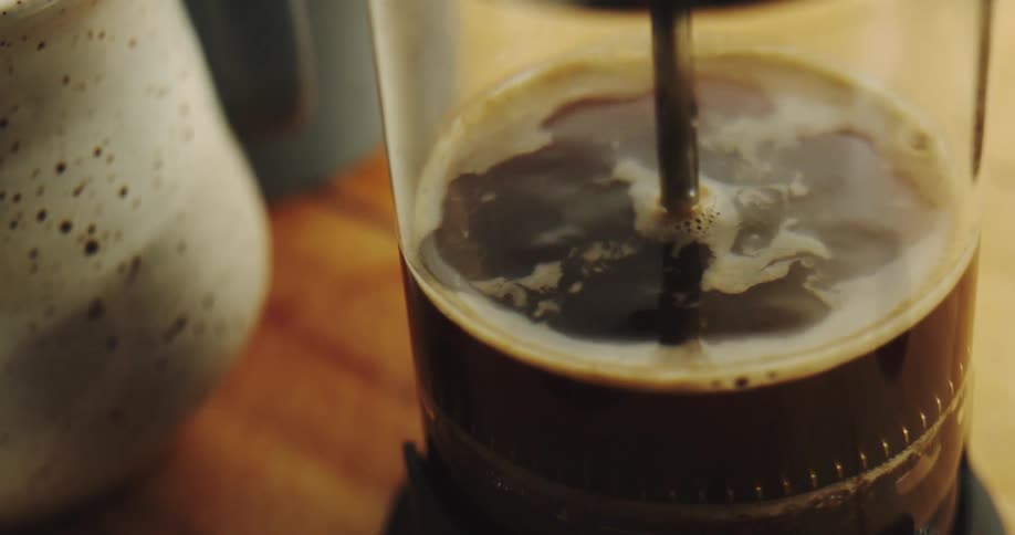 A slow-motion close-up of a French press being plunged to brew fresh coffee