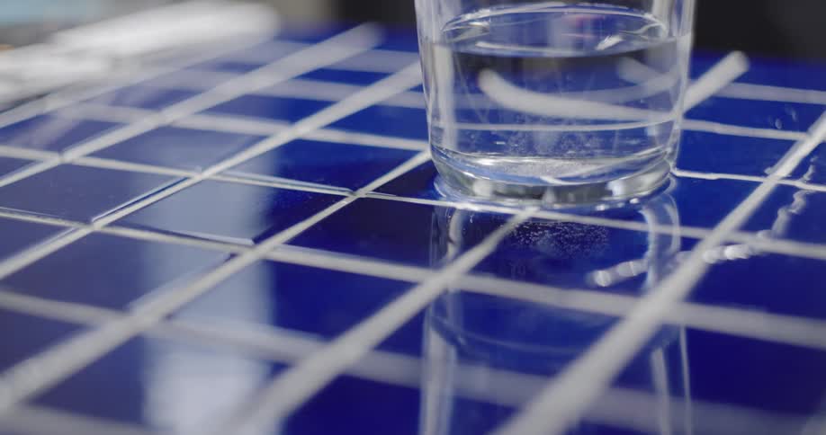 Close-up of a fizzy antacid tablet dissolving in a glass of water on a blue tiled surface