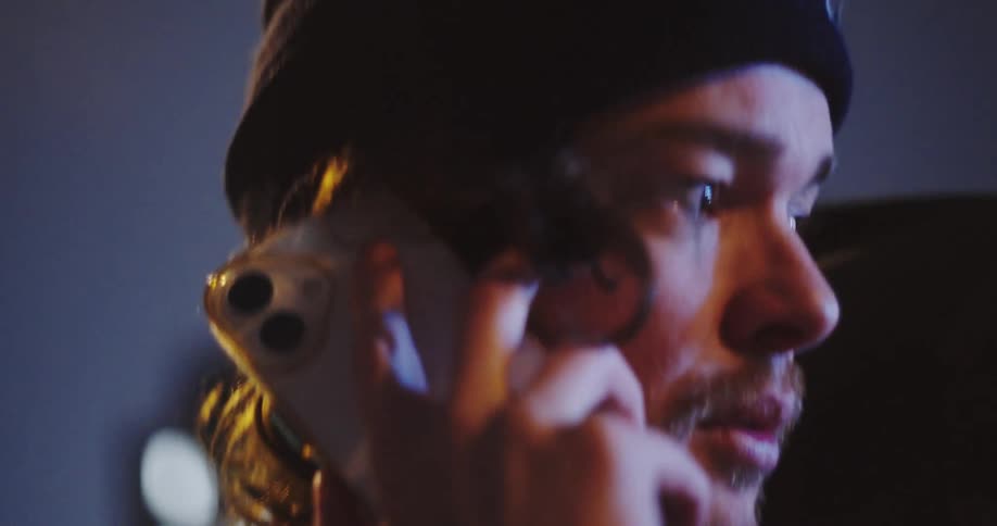 Cinematic close-up of a young man in a beanie talking on his mobile phone on a city street at night
