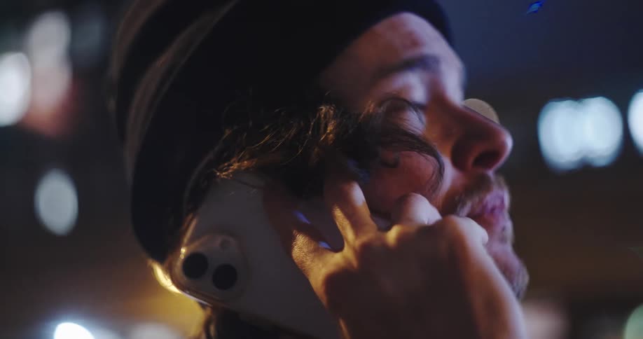 A close-up shot of a young man on a serious phone call at night, with the glow of city lights in the background