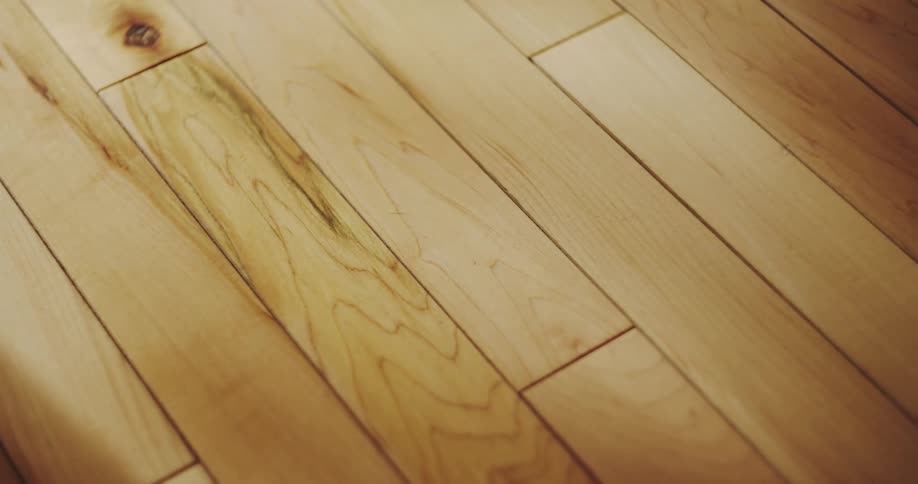 A static close-up of a light-colored hardwood floor with soft light slowly passing over the wood grain