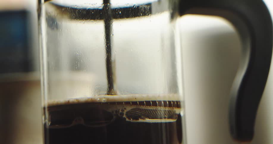 A close-up, slow-motion shot of a French press plunger being pushed down to filter fresh coffee