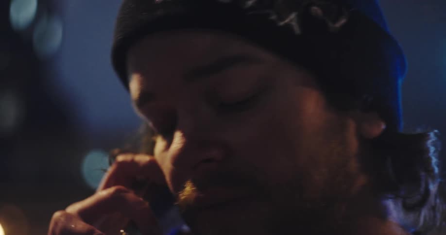 A dramatic slow-motion close-up of a serious man on a phone call at night, illuminated by cool-toned city lights