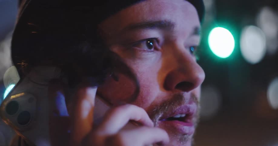A close-up shot of a young man having an emotional phone conversation at night on a city street in slow motion