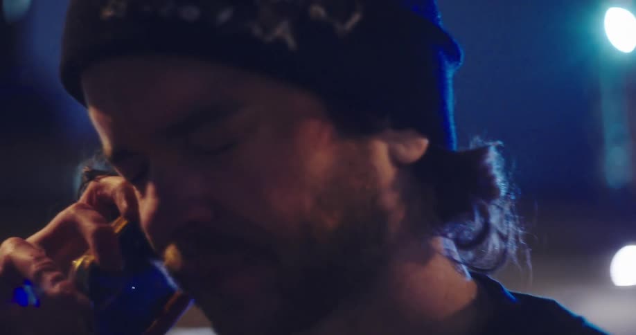 A young man wearing a beanie receives devastating news over the phone and begins to cry at night